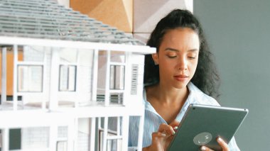 Genç, güzel İspanyol mimar mühendis modern ofisteki ev modeli yapısını kontrol ederken tablet kullanarak bina inşaatını çiziyor. Yaratıcı iş inşaat konsepti. Yönlendirici.