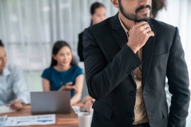 İş adamı, toplantı odasının arka planında çeşitli iş arkadaşlarıyla güven içinde poz veriyor. Çok kültürlü ekip iş başarısı için birlikte çalışır. Modern iş adamı portresi. Uyum