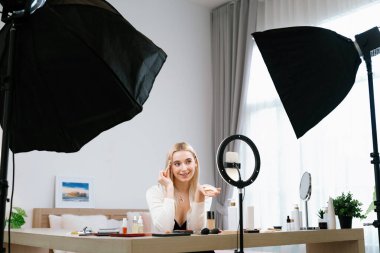 Sosyal medya için güzellik ve kozmetik video içeriği hazırlayan genç bir kadın. Güzellik blogcusu kameraya gülümserken seyirciye ya da takipçilere güzellik teninin nasıl uygulanacağını gösteriyor. Blithe