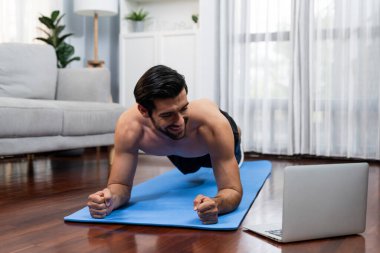 Atletik ve sporcu adam, evdeki formda fiziğe ve sağlıklı spor yaşam tarzına uygun vücut egzersizi sırasında spor minderinde kalas yapıyor. Gaiety evde egzersiz eğitimi.