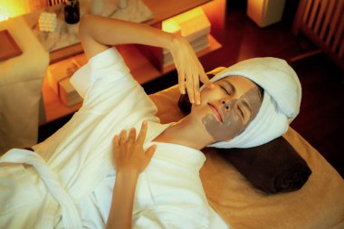 Kaplıca salonunun sakin atmosferi, üst düzey kadın müşteri sıcak mum ışığında kömür kömürü yüz kremi masajıyla kendini yenilemeye çalışıyor. Yüz bakımı ve güzellik konsepti. Sessiz.