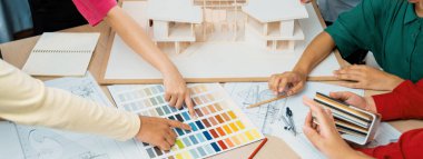 Yetenekli mimar takımı ev inşaatı hakkında tartışırken, iç mimar ev modeli ve bina planının dağıldığı renk paletine uygun bir renk belirliyor. Üst Manzara. Değiştirilmiş.