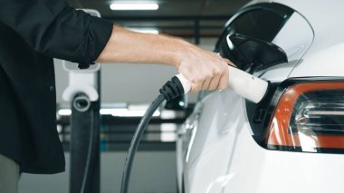 Genç adam EV elektrikli arabasıyla şehir merkezindeki alışveriş merkezinin otoparkına gidiyor şehir merkezindeki sürdürülebilirlik yaşam tarzını yeşil, temiz, yeniden şarj edilebilir elektrikli araç iç organlarıyla şarj ediyor.