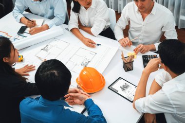 Mimari proje üzerinde birlikte çalışan çeşitli inşaat mühendisi ve müvekkil grupları, toplantı masasında tablet kullanarak inşaat planını gözden geçirip bina planı hazırlıyorlar. Tedbirli