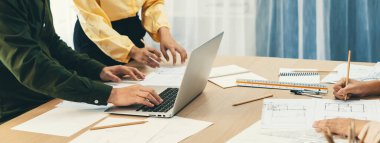 Profesyonel mimar dizüstü bilgisayar kullanarak projeyi düzenlerken proje yöneticisi de toplantı masasının üzerindeki toplantı masasında mimari dökümanların etrafa dağıldığı noktayı işaret etti. - Yakın çekim. Tanımlama.