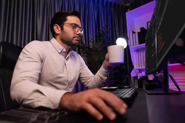 Smart IT developer drinking coffee cup while working in software development coding on pc screen, presenting program application update online website database at neon lighting cyber office. Surmise.