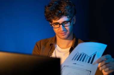 Genç işadamı, Neon Light Modern Ofis 'teki yeni proje surround çalışma masası için kağıt üzerinde tasarım düşünüyor. E-posta ile hediye göndermeden önce not defterine yeni bir iş düşünüyorum. Toplayıcı.