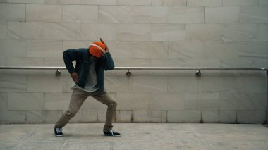 Asyalı akıllı hipster, kulaklık ve şık kıyafetler giyip hip hop şarkıları dinlerken gri arka planlı enerjik break dans gösterisi yapıyor. Açık hava sporu 2024. Hip hop hareketi. Yumuşak bir şekilde..