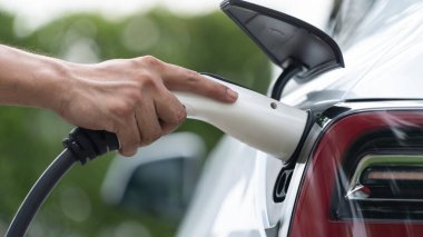 Yakından el yerleştirme ve şarj etmek için EV şarj cihazı şarj istasyonundan şarj ediliyor. Alternatif enerji, gelecekteki sürdürülebilirlik için çevre dostu taşımacılığında kullanılıyor. Eşzamanlama