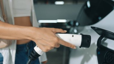 Genç hareketli kadın, EV elektrikli arabasıyla şehir merkezindeki alışveriş merkezinin otoparkına gidiyor. Sürdürülebilirlik yaşam tarzını yeşil, temiz, yeniden şarj edilebilir elektrikli araç iç organlarıyla şarj ediyor.
