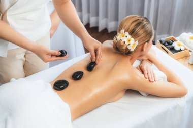 Lüks tatil köyündeki kaplıcalarda sıcak taş masajı. Gün ışığı sükunet ortamında, mutlu kadın müşteri bazalt taş masajından zevk alıyor. Rahatlatıcı bir sıcaklıkla vücudun üzerinde süzülüyor. Sessiz.