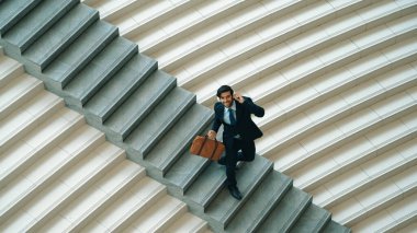 Kameraya bakarken kulaklıktan müzik dinleyen bir iş adamı görüntüsü. Yetenekli proje yöneticisi kameraya gülümserken merdivenlerden iniyor. Beyaz arka plan. Modern dans. Sevinçli..