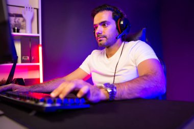 Akıllı oyun kurucusu, dijital neon ışıklandırma stüdyosundaki sosyal medya uygulamasında başkalarıyla iletişim kurmak için kulaklık ve mikrofon kullanan takım üyeleriyle konuşuyor. Tahmin et..