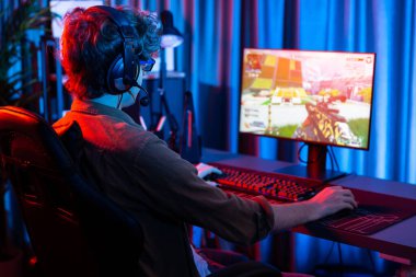 Genç oyun flamasının sunucu kanalı, takım oyuncusu, dijital neon odasında mikrofonlu kulaklık takarak bilgisayar ekranında çoklu oyuncuyla savaş oyunu oynuyor. Toplayıcı.