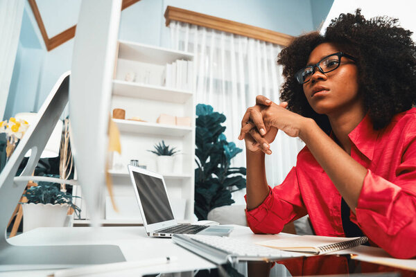 Young African businesswoman focusing project on screen monitor laptop, researching information data center on website pc and smartphone. Theme of place work in comfy room with plain color. Tastemaker.