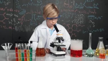 Akıllı çocuk BTMM bilim sınıfında ya da kimya dersinde mikroskop analiz numunesi kullanıyor. Kafkasyalı mutlu öğrenci tüplerdeki kimyasal sıvıyı incelemek için mercek altına bakıyor. Etkinlik.
