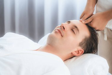 Beyaz adam stres önleyici kafa masajından ve lüks bir tatil beldesi veya otel spa salonundaki modern ışık ortamında yüz güzelliği eğlencelerini şımartmaktan hoşlanıyor. Sessiz.