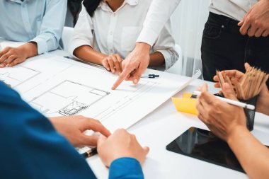 Mimari proje üzerinde birlikte çalışan çeşitli inşaat mühendisi ve müvekkil grupları, inşaat planını gözden geçirip toplantı masasında plan oluşturuyorlar. Tedbirli