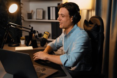 Sunucu kanalı akıllı yayıncı laptopta canlı sosyal medya uygulaması arıyor, kulaklık takıyor ve modern ofis stüdyosundaki mikrofonu kullanıyor. Bireysel.