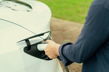 Açık yeşil şehir parkı manzaralı EV şarj istasyonundan EV elektrikli araçları şarj eden adam. Çevre dostu şehir ulaşımı ve çevre dostu EV araba seyahati. Yükselt