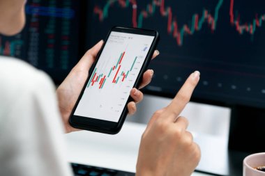 Modern ofisteki bilgisayar ekranlarıyla karşılaştırıldığında borsa grafiği üzerinden akıllı telefon kullanan bir iş kadınında kesilmiş görüntü. Zenginlik güvenliğine yüksek kar yatırımı kavramı. Taktik.