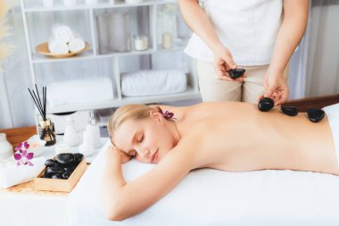 Lüks tatil köyündeki kaplıcalarda sıcak taş masajı. Gün ışığı sükunet ortamında, mutlu kadın müşteri bazalt taş masajından zevk alıyor. Rahatlatıcı bir sıcaklıkla vücudun üzerinde süzülüyor. Sessiz.