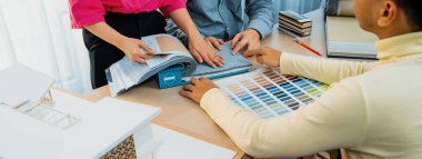 Yetenekli iç dizayn ekibi perde malzemelerini dikkatle seçerken iş arkadaşı da toplantı masasının üzerinde ev modeliyle perdenin rengini seçiyor. Yaratıcı tasarım konsepti. Değiştirilmiş.