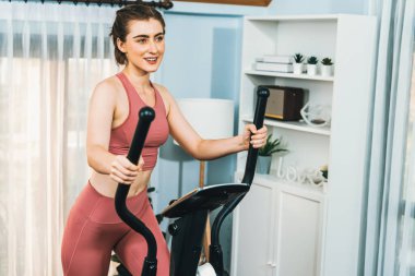 Spor ve atletik bir kadın, evdeki fiziğe ve sağlıklı spor yaşam tarzına uygun vücut egzersizi sırasında eliptik koşu makinesiyle koşuyor. Gaiety evde egzersiz eğitimi.