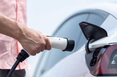 Dışarıdaki şarj istasyonundan EV şarj aletini şarj etmek için elektrikli araca elle tak. Alternatif temiz ve sürdürülebilir enerji kavramına sahip taze gün ışığı ortamı. Kalıcı