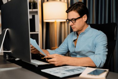 Akıllı iş adamı iş paragrafı dinamik pazarlama analizi planını analiz ediyor. Kağıt kağıtları ve bilgisayar monitörü raporlarını gece evdeki belge verileriyle karşılaştırmak için hazırlıyor. Bireysel.