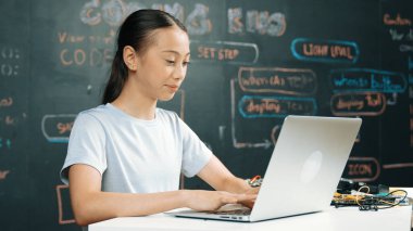 Kara tahtada dizüstü bilgisayar kullanarak akıllı kız programlama sistemi. Lise öğrencisi BTMM teknoloji sınıfında ekrana bakarken mühendislik kodu yazıyor. Yaratıcı eğitim. Öğretim.