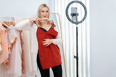 Genç sosyal medyum kadın moda videosu yapıyor. Blogcu kameraya ve ışık çemberine gülümserken, aynı zamanda ikna edici çevrimiçi kıyafetleri izleyicilere veya takipçilere vlog sattırıyor. Blithe