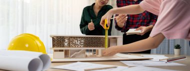 Akıllı mimar mühendis ve iç mimar birlikte çalışıyor ve ev modelini ölçmek için plan ve mimari ekipmanlarla toplantı masasında cetvel kullanıyor. Takım çalışması konsepti. Filizlenen.