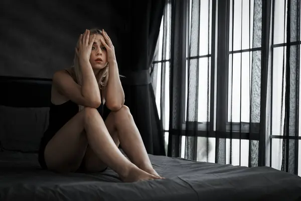 Young woman with critical depression and anxiety disorder from loneliness, mental sickness, or unwanted pregnancy, cuddling herself on dark bedroom. Overwhelming negative thought. Blithe