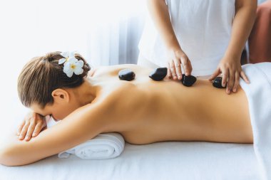 Lüks tatil köyündeki kaplıcalarda sıcak taş masajı. Gün ışığı sükunet ortamında, mutlu kadın müşteri bazalt taş masajından zevk alıyor. Rahatlatıcı bir sıcaklıkla vücudun üzerinde süzülüyor. Sessiz.