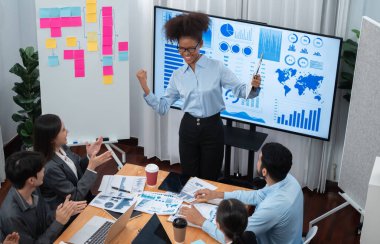 İş adamları TV ekranında başarılı bir sunum veya veri analizi toplantısından sonra kutlama yapıyorlar. Mutlu takım ofis odasında toplanıyor, kutlama jestleriyle işbirliği için tezahürat yapıyorlar. Uyum