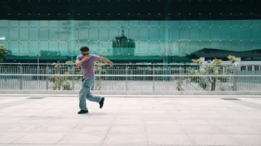 Asyalı hipster şehirde kameraya bakarken dondurucu poz veriyor. Profesyonel sokak dansçısının panorama çekimi B-boy ayak dansı ya da break dans. Modern yaşam tarzı. Açık hava sporu 2024. Yumuşak bir şekilde..