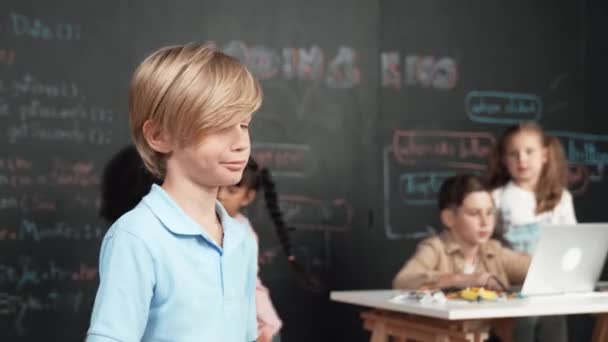 親指を示すスマートな少年は 多様な友人が働いている間 またはエンジニアリングコードを学ぶか Stemテクノロジークラスルでプロンプト 子供がノートパソコンを使っている間 カメラに立っている白人学生 エラー — ストック動画