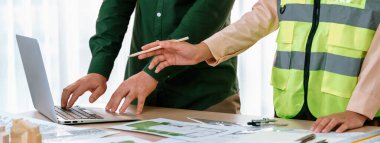 Mimarlık ve güvenlik mühendisi, modern ofiste dizüstü bilgisayarda mimari belge ve ahşap blokla sergilenen planlar hakkında tartıştı. - Yakın çekim. Tanımlama.