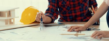 Kooperatif mimar ekibinin kesilmiş görüntüsü ev modeli, güvenlik miğferi ve mimari planlarla toplantı masasında birlikte çalışmaya karar verir ve birlikte çalışırlar. - Yakın çekim. Eline odaklan. Filizlenen.