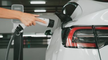 Genç adam EV elektrikli arabasıyla şehir merkezindeki alışveriş merkezinin otoparkına gidiyor şehir merkezindeki sürdürülebilirlik yaşam tarzını yeşil, temiz, yeniden şarj edilebilir elektrikli araç iç organlarıyla şarj ediyor.