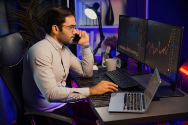 Tüccar akıllı işadamı komisyoncuyu ya da ortağını arıyor, modern evde kârlı bir finans teknolojisi olan neon aydınlatma ofisindeki bilgisayardaki dinamik borsa yatırımlarını analiz ediyor. Tahmin et..