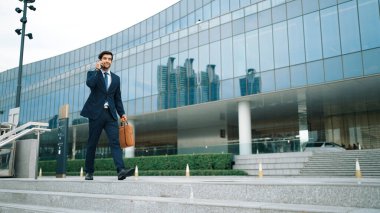 Akıllı iş adamı binada yürürken telefonla konuşuyor. İş planı, pazarlama stratejisi ya da çalışma hakkında konuşmak için akıllı telefonla konuşurken sokakta yürüyen mutlu bir yönetici. Sevinçli..