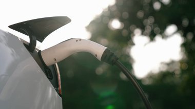 Elektrikli araç EV şarj prizine bağlı yakın çekim EV şarj cihazı EV şarj istasyonundan gündoğumu ya da günbatımı aydınlatması ile elektrik şarj ediyor. Yükselt