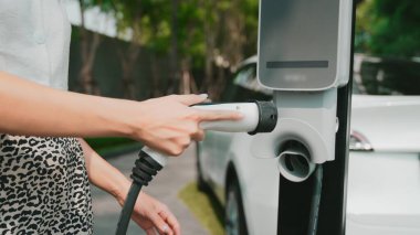 Genç bir kadın yazın yeşil sürdürülebilir şehir bahçesinde EV elektrikli arabasıyla seyahat ediyor. Kentsel sürdürülebilirlik yaşam tarzı yeşil temiz yeniden şarj edilebilir enerji elektrikli BEV araç iç organları