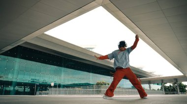 Serbest dans ederken müzik dinleyen profesyonel hipsterin hareketli çekimi. Sokak dansçısı hareket ediyor, el sallıyor ve break dansın tadını çıkarıyor. Modern yaşam tarzı. Açık hava sporu 2024. Yumuşak bir şekilde..