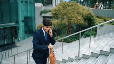 Gülümseyen yakışıklı iş adamı, parkın merdivenlerinde yürürken aynı zamanda işletme müdürünü arıyor. Yatırımcı işe giderken meslektaşıyla konuşuyor. Sevinçli..