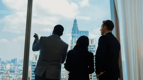 背景には 街並みのスカイラインへの窓を眺める装飾されたオフィスに立っている野心的なビジネスの人々の多様なチームがあります 決意とビジネスの野心が明るい未来に向かってキャリアを推進する — ストック写真