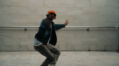 Asyalı akıllı hipster, kulaklık ve şık kıyafetler giyip hip hop şarkıları dinlerken gri arka planlı enerjik break dans gösterisi yapıyor. Açık hava sporu 2024. Hip hop hareketi. Yumuşak bir şekilde..