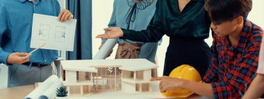 Yetenekli mimar mühendis ekibi proje yöneticisine ev yapımı sunarken, iş arkadaşı da ev planını gösteriyor. Profesyonel yönetici toplantı odasında ev inşaatını tartışıyor..